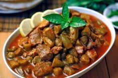 a bowl filled with meat and vegetables on top of a wooden table next to lemon wedges