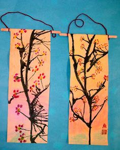 two paintings hanging from clothes pins on a blue background, each with an image of a tree and bird