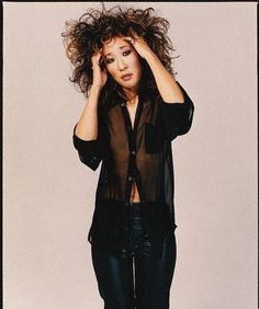 a woman with her hair blowing in the wind, wearing black pants and a sheer shirt