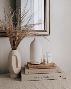 a white vase sitting on top of two books next to a mirror and some plants