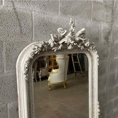 an ornate white mirror sitting on top of a floor next to a wall with a chair in it