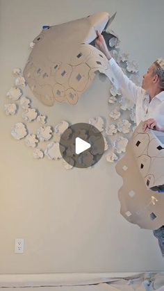 a woman in white shirt and blue jeans painting a wall with paper flowers on it