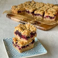 blueberry crumb bars are stacked on a plate next to a tray with one slice cut out