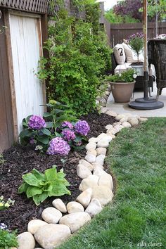 a garden with rocks and flowers in the grass near a fenced in area that has an umbrella over it