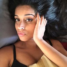 a woman laying on top of a bed with her hand under her head and looking at the camera