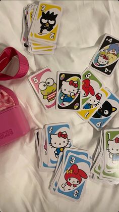 hello kitty playing cards are laying on a bed with a pink purse and other items