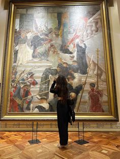 a woman standing in front of a painting with people on it's sides looking at it