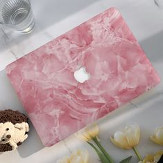 a pink marble macbook cover with a teddy bear and flowers on the table next to it