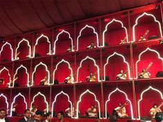 a group of people sitting in front of a red shelf with guitars on top of it