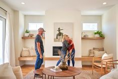 a man and woman standing in front of a living room with a fire place on the wall