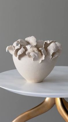 a white bowl filled with lots of flowers on top of a table next to gold legs