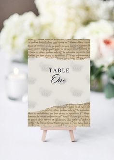 a table sign sitting on top of a wooden easel next to white and pink flowers