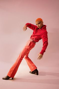 a man in orange pants and a red hoodie is posing with his arms outstretched