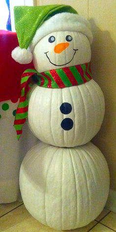 a snowman sitting on top of a white pumpkin next to a red and green pillow