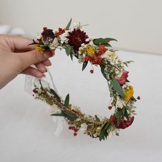 a hand holding a flower crown made out of flowers and greenery on a white surface