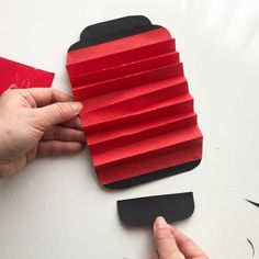 someone is making a paper car out of red and black pieces of construction paper with scissors