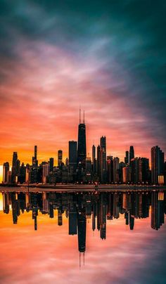 a city skyline is reflected in the water at sunset, with colorful clouds and bright colors