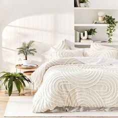 a bed with white comforter and pillows in a room next to a potted plant