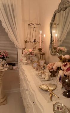 a white table topped with lots of vases filled with pink flowers and candles next to a mirror