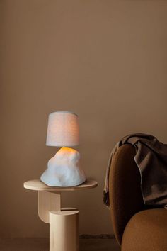 a lamp sitting on top of a table next to a brown chair and a pillow