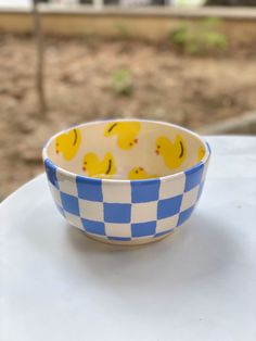 a blue and white checkered bowl with yellow rubber ducks on it sitting on a table