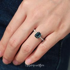 a woman's hand wearing a ring with an emerald colored stone and diamond accents