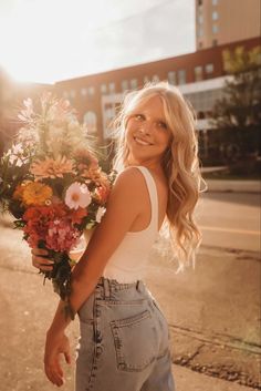 a woman holding a bunch of flowers in her hand on the side of the road