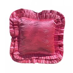 a pink pillow with ruffled edges and a decorative design on the back, sitting in front of a white background