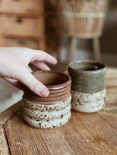 a person is reaching for something in a jar on top of a wooden table next to another cup