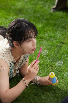 a woman laying on the grass blowing bubbles with her pink toothbrush in her hand