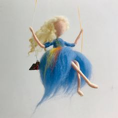 a doll hanging from a string with a blue dress and long blonde hair on it's back