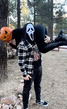 a person wearing a mask and holding a pumpkin in front of their face while standing next to a tree