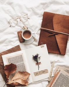 an open book, cup of coffee and some leaves on a white sheet with eyeglasses