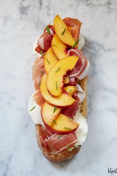 a sandwich with peaches and prosciutto on it sitting on a marble surface