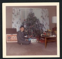 a man sitting on the floor in front of a christmas tree