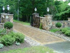 an entrance to a home with stone pillars and gates, surrounded by greenery in the foreground