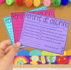 a hand holding three spanish id cards in front of a bulletin board with pom poms