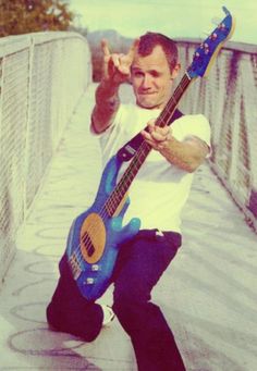 a man is sitting on a bridge with his guitar and giving the peace sign while holding it in one hand