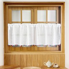 a teapot and cup on a table in front of a window with white curtains