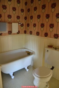 a white toilet sitting next to a bath tub in a room with floral wallpaper