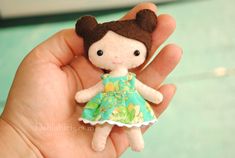 a hand holding a small doll with brown hair and green dress on it's head