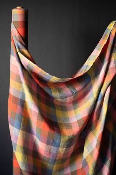 an orange, yellow and blue plaid blanket draped over a black wall with a roll of thread