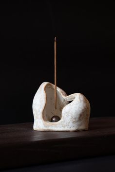 a small white sculpture with a wooden stick sticking out of it's mouth, sitting on a table