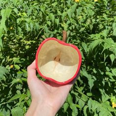 a hand holding an apple in front of some green plants