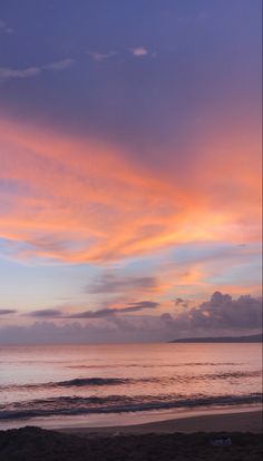 a person walking on the beach with a surfboard under a pink and blue sky