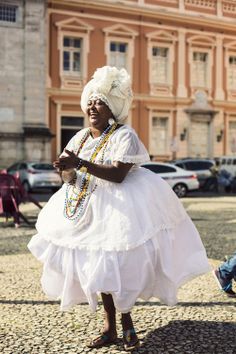 a woman in a white dress and headdress is dancing on the street with other people