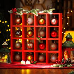 a red shelf filled with christmas ornaments on top of a wooden table next to a lit candle