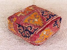 a red and blue rug on the floor with a small square shaped ottoman in front of it