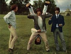 three men standing in the grass with their hands up and one man upside down on his head