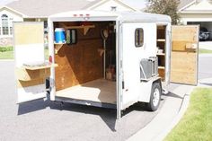 an enclosed trailer parked on the side of a road in front of a house with its doors open